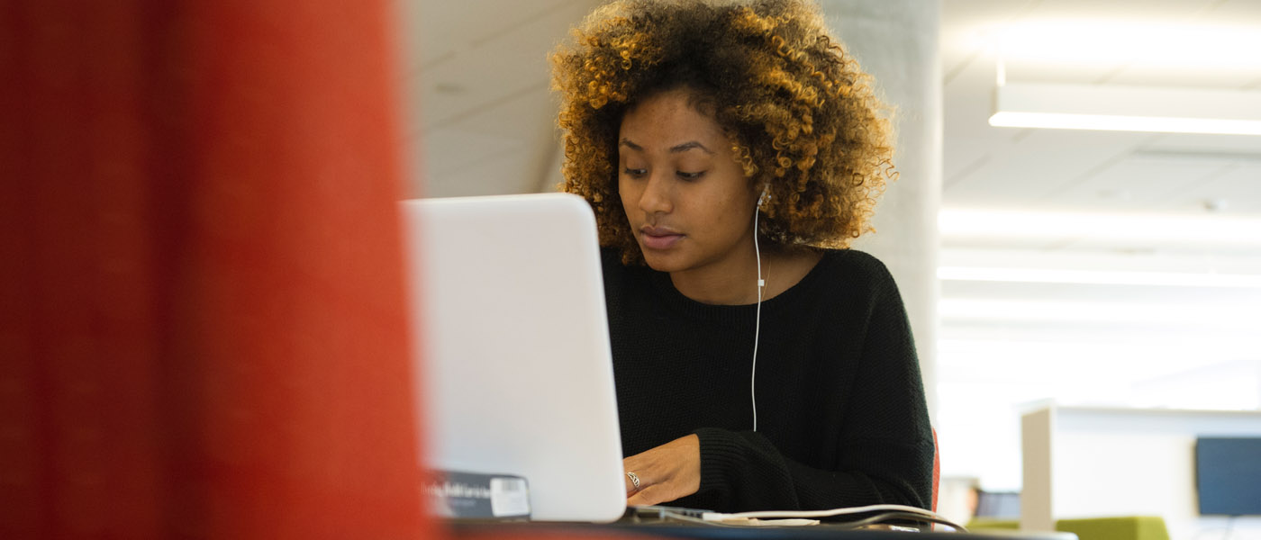 A black woman wearing a black t-shirt works at a computer while wearing headphones