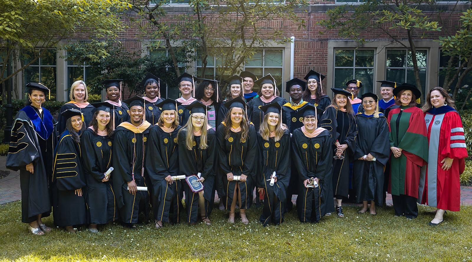 A group of 25 people in commencement robes pose for a photograph